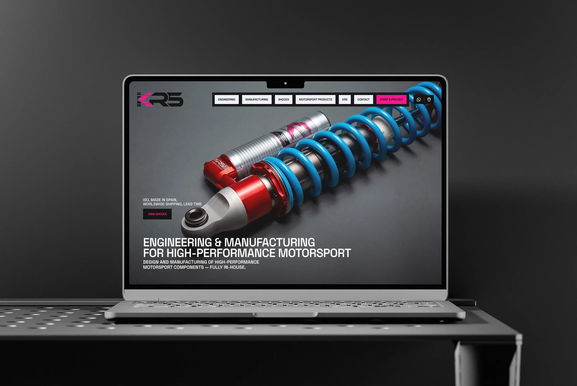 Web de KRS Racing Systems presentada en un portátil con un amortiguador de competición